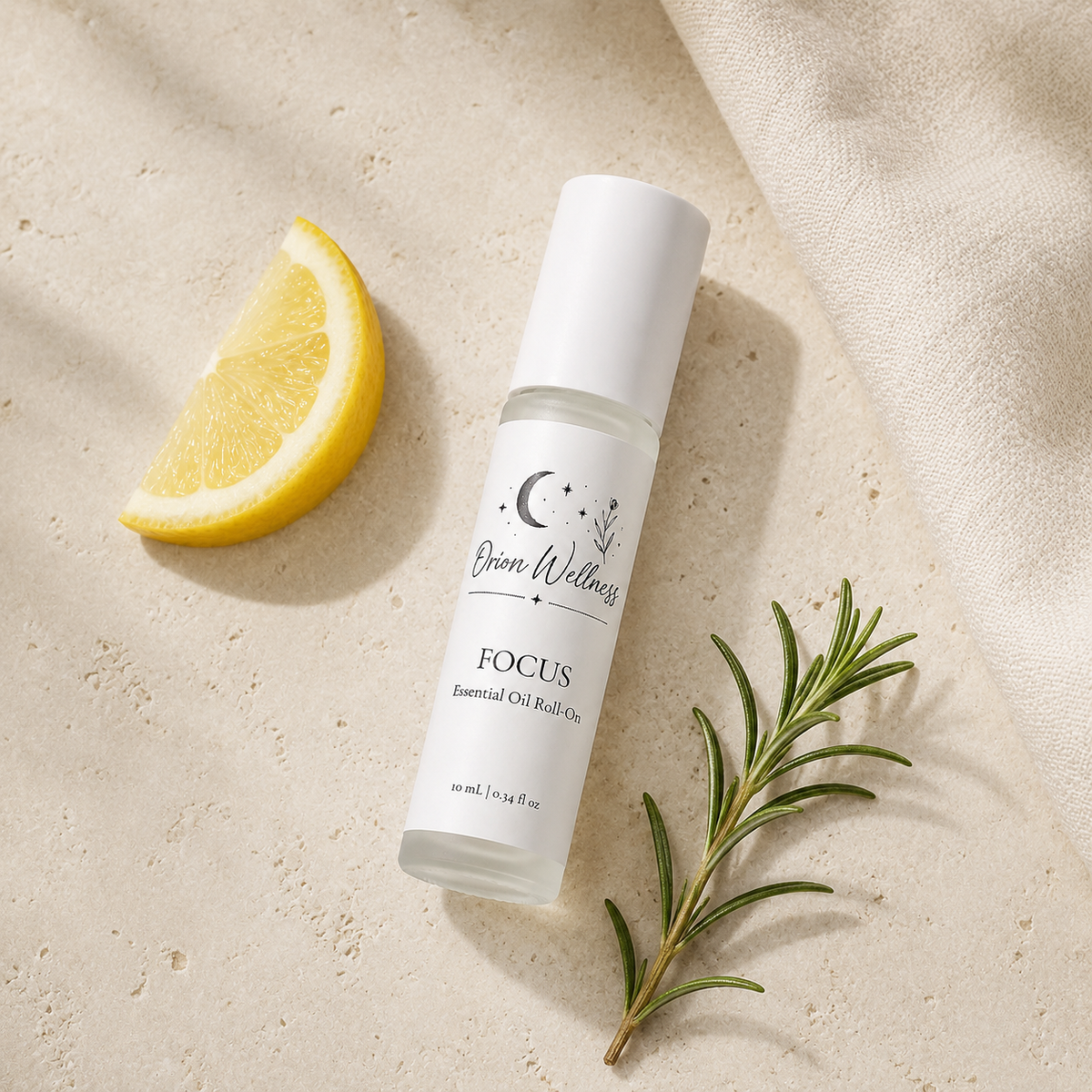 Orion Wellness Focus 10 mL roll-on on pale stone beside a lemon wedge, rosemary sprig, and ivory linen.