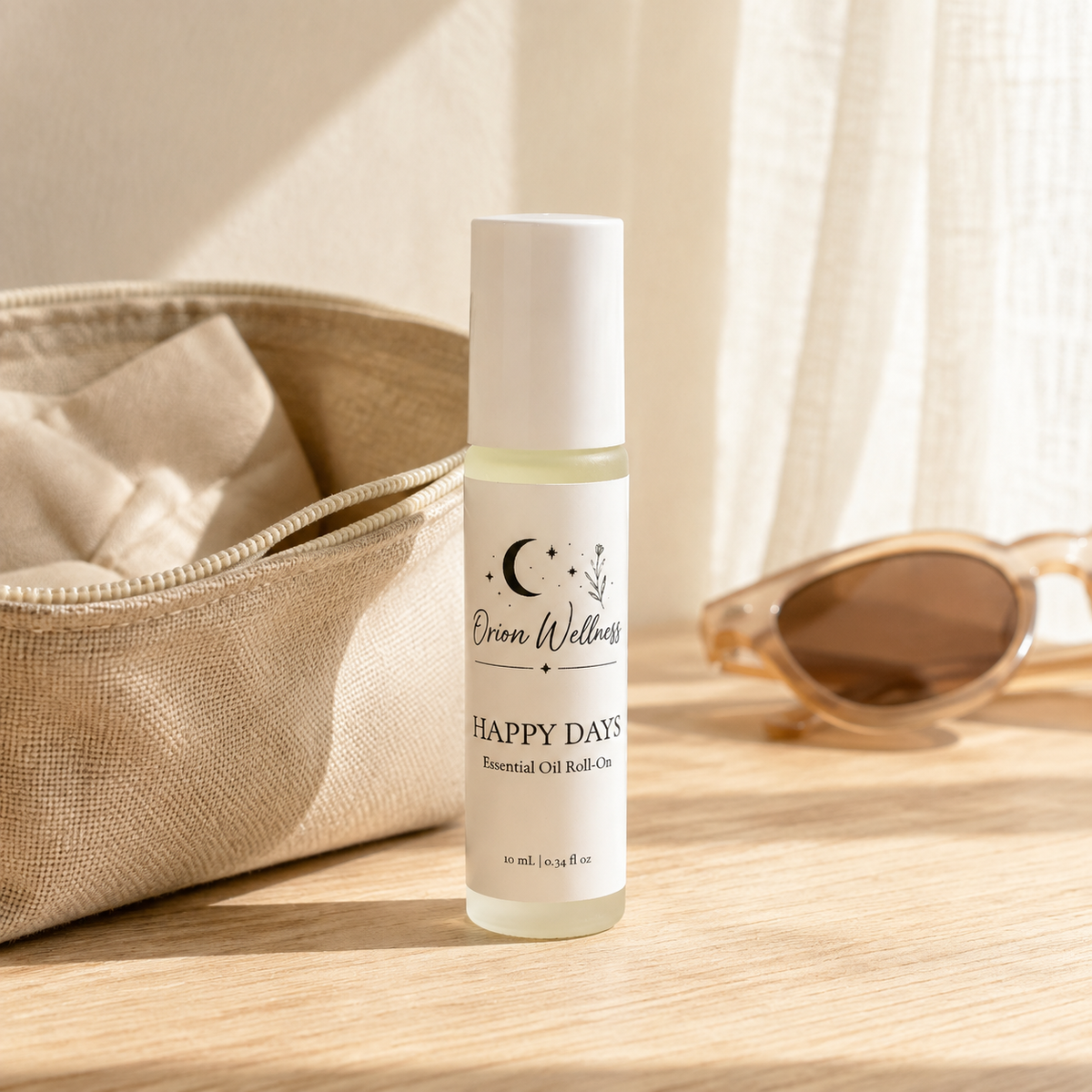 Orion Wellness Happy Days roll-on beside a natural linen pouch and sunglasses in warm window light.