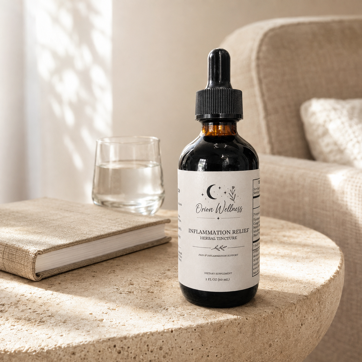 Orion Wellness Inflammation Relief tincture on a pale stone side table beside a glass of water and a linen-covered book in soft window light.