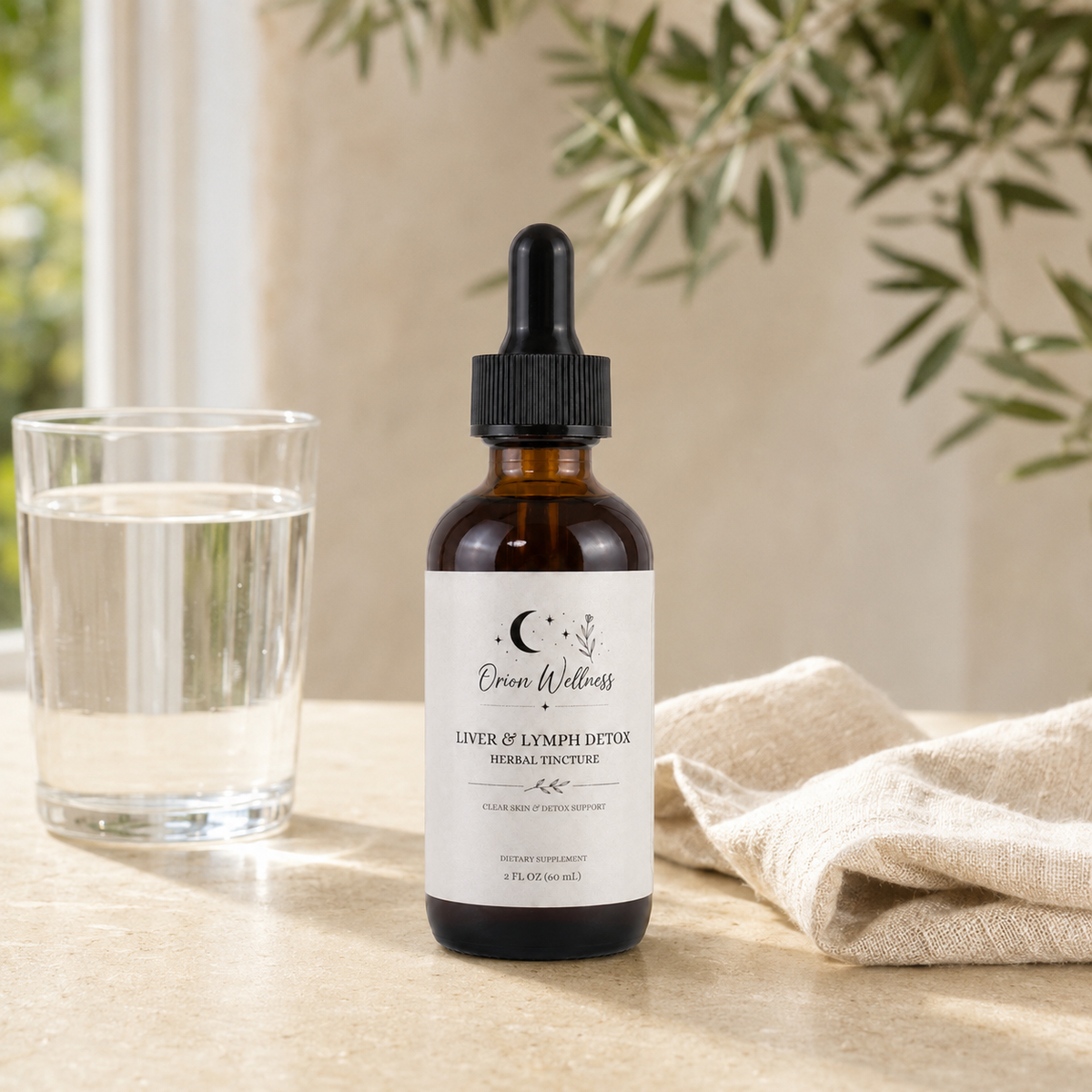 Orion Wellness Liver & Lymph Detox tincture on a pale stone kitchen counter with a clear water glass, neutral linen, and soft greenery behind.